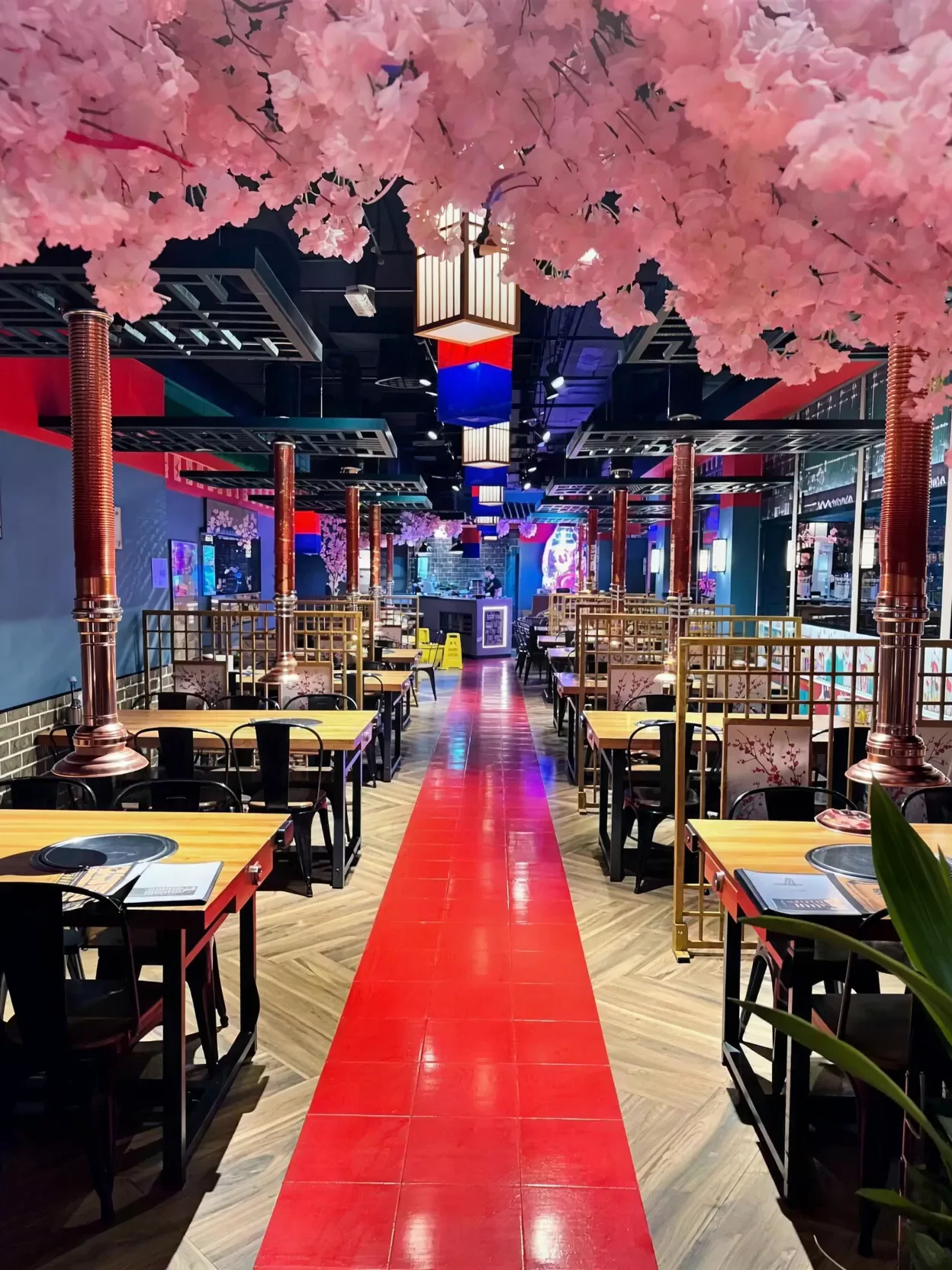 Mukbang Shows Korean BBQ dining hall with cherry-blossom ceiling leading to a sizzling table-top grill and banchan spread