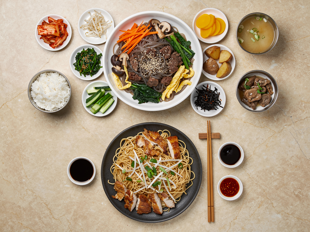 Japchae vs Chow Mein (2026): The Honest UAE Guide 3 Korean table with japchae, banchan and rice beside a plate of chicken chow mein with bean sprouts