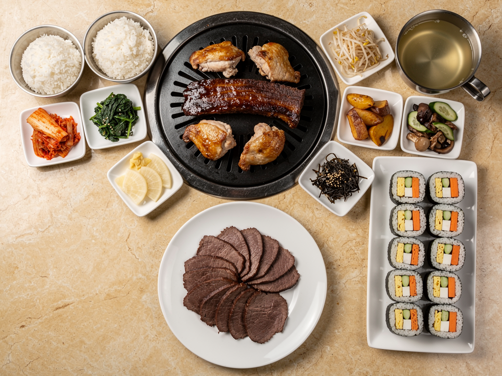 Korean barbecue table spread with banchan, rice and soup alongside a plate of carved roast beef