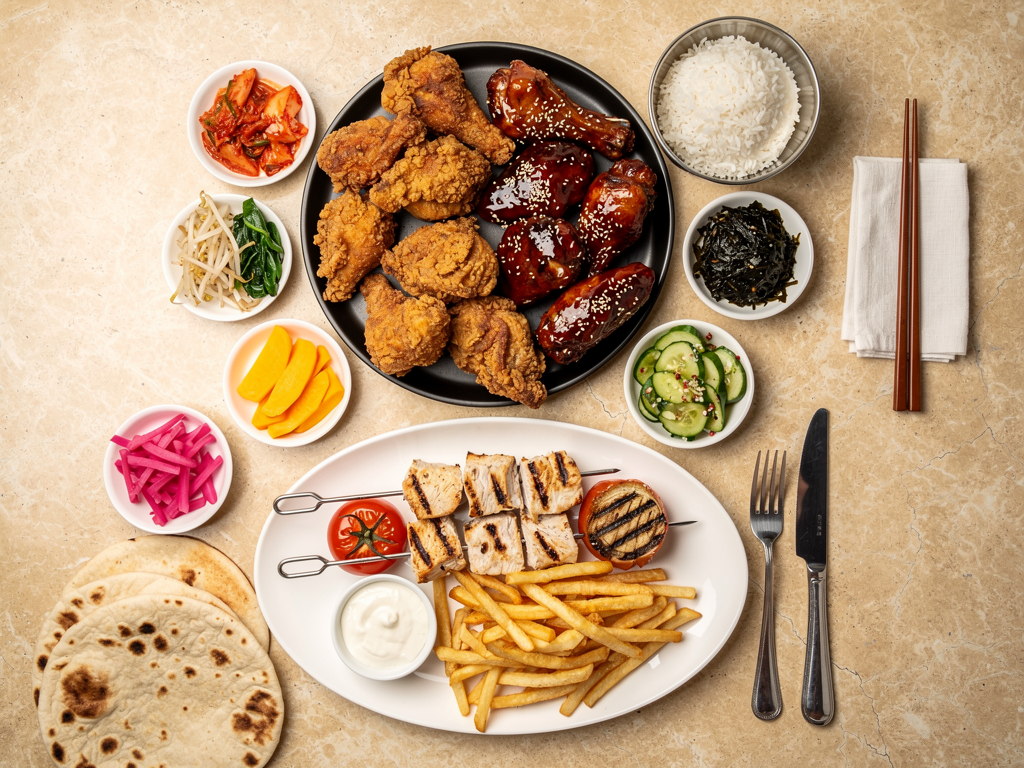 Overhead table spread comparing a Korean fried chicken platter with a shish tawook plate