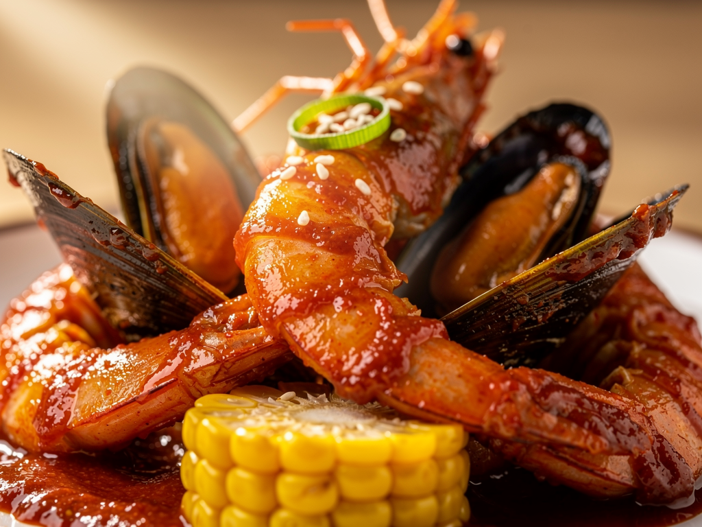 Close-up of prawns and mussels coated in thick red Korean gochujang boil sauce